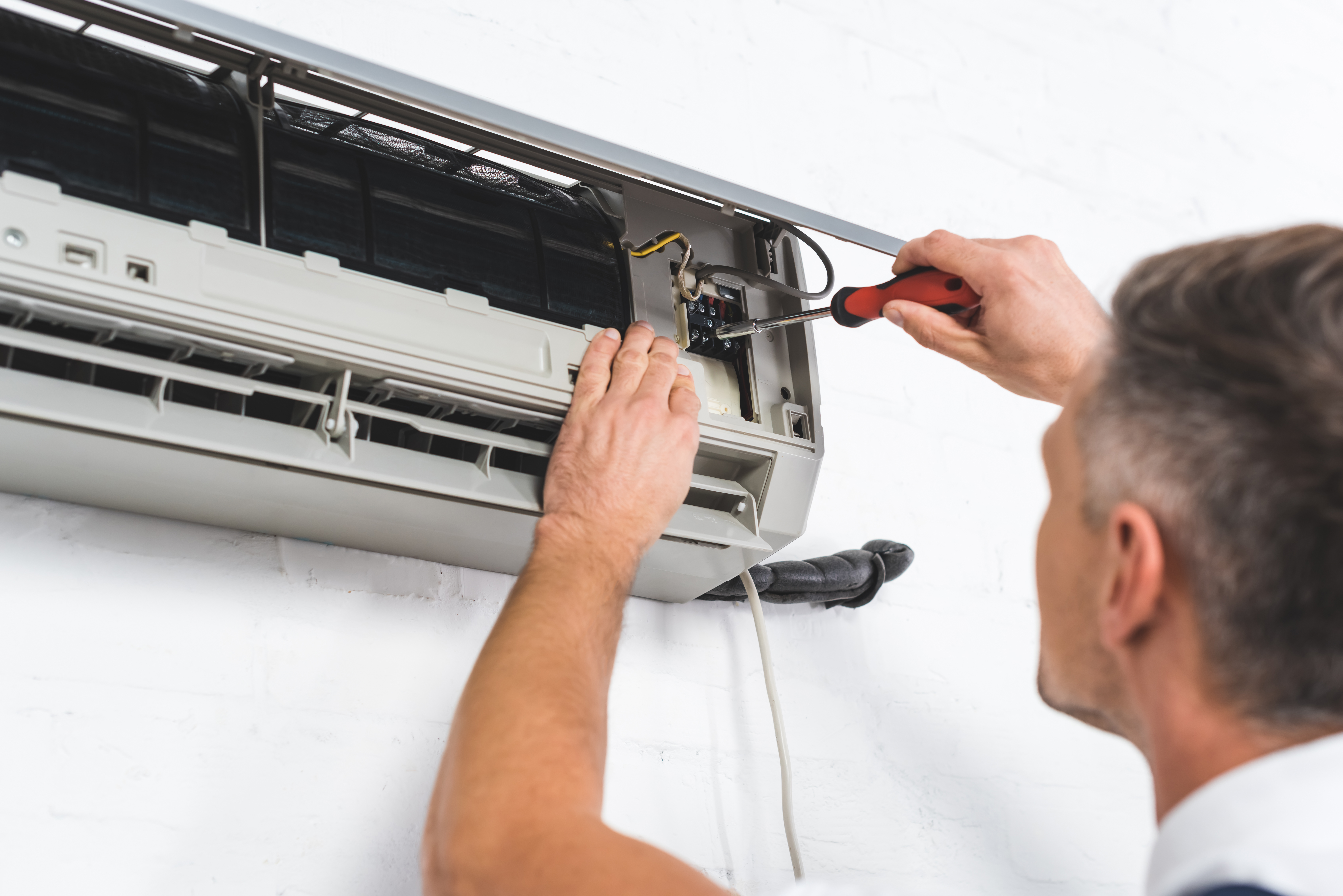 Close up view of an adult repairman repairing an wall mounted air conditioning unit